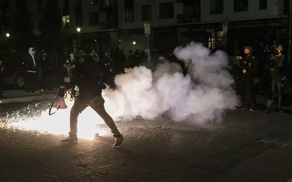 A cloud of tear gas silhouetting human figures against a night sky in downtown Portland, OR