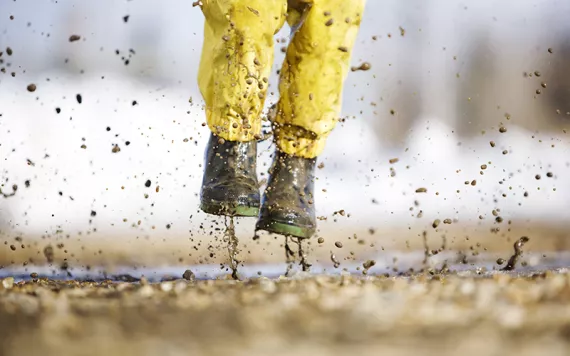 Child photographed from the waist down jumping into a puddle with yellow pants and black rain boots