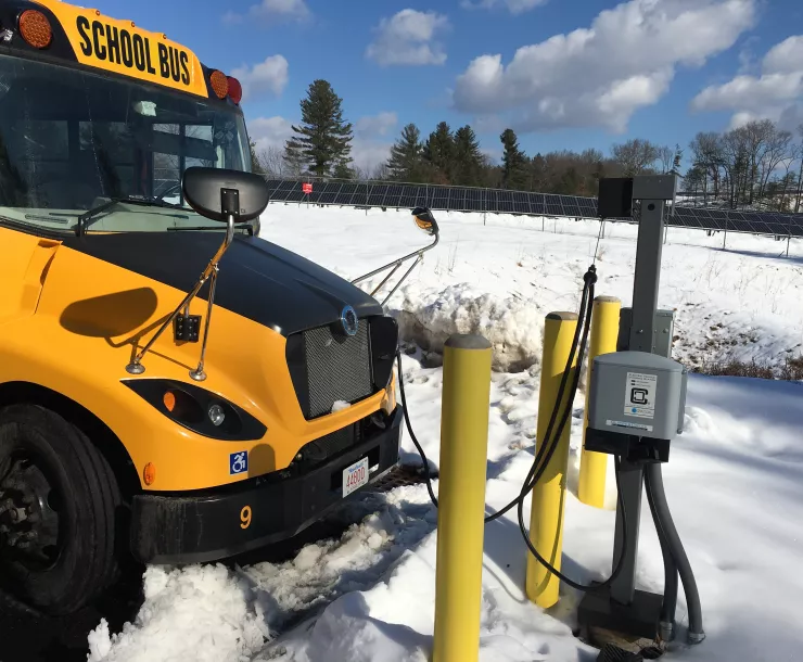 A charging school bus surrounded by snow