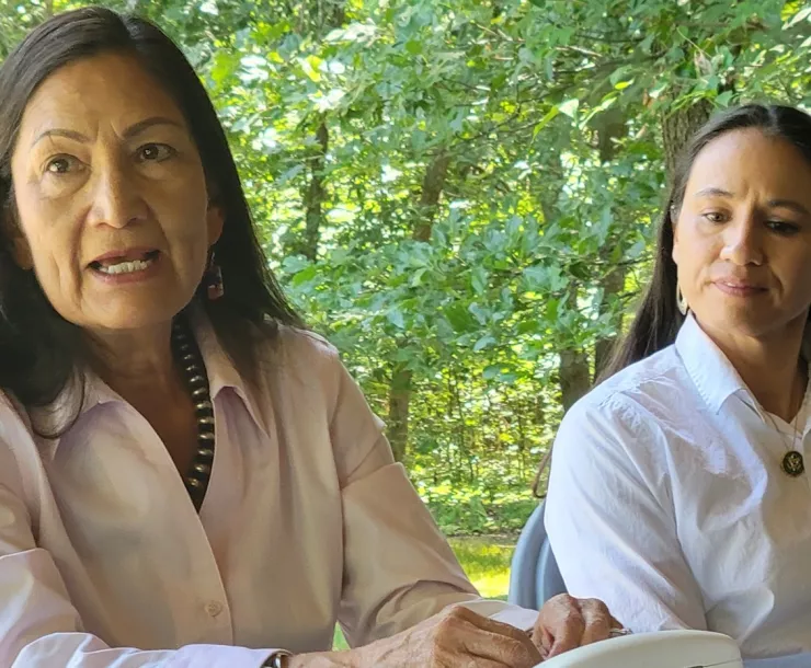 Two women side by side with green trees in background