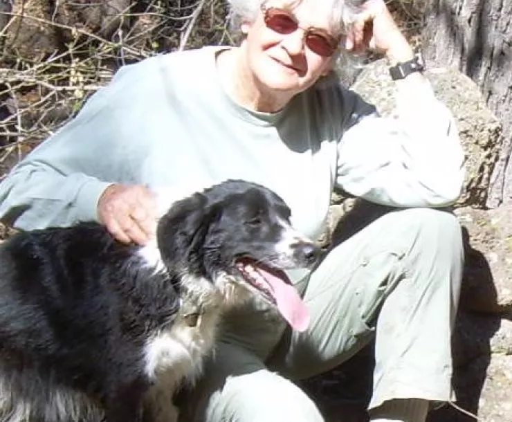 woman in jeans and hiking boots sitting in woods with black and white dog