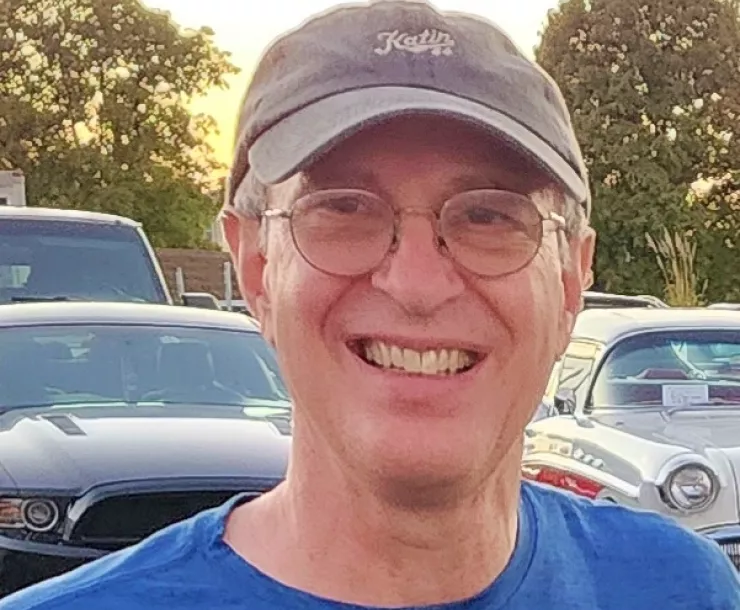 A man with a grey baseball cap and glasses smiling for the camera.