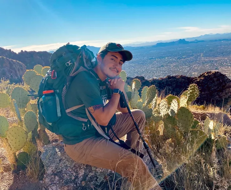 Miché Lozano sitting on a rock wearing a backpack atop a mountain
