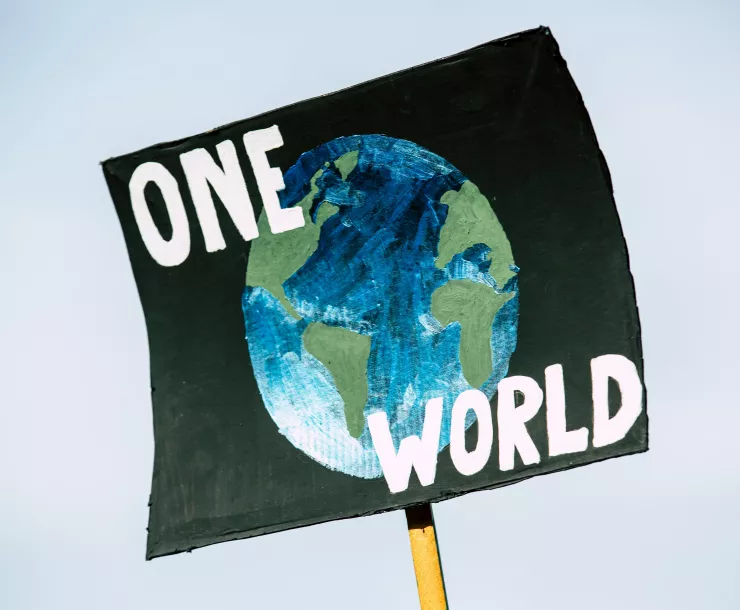 A sign with the words "One World" superimposed on a drawing of the Earth is held in the sky.