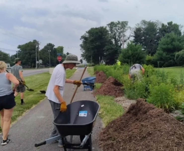 Four people working on a pollinator path. One person is by a wheelbarrow.