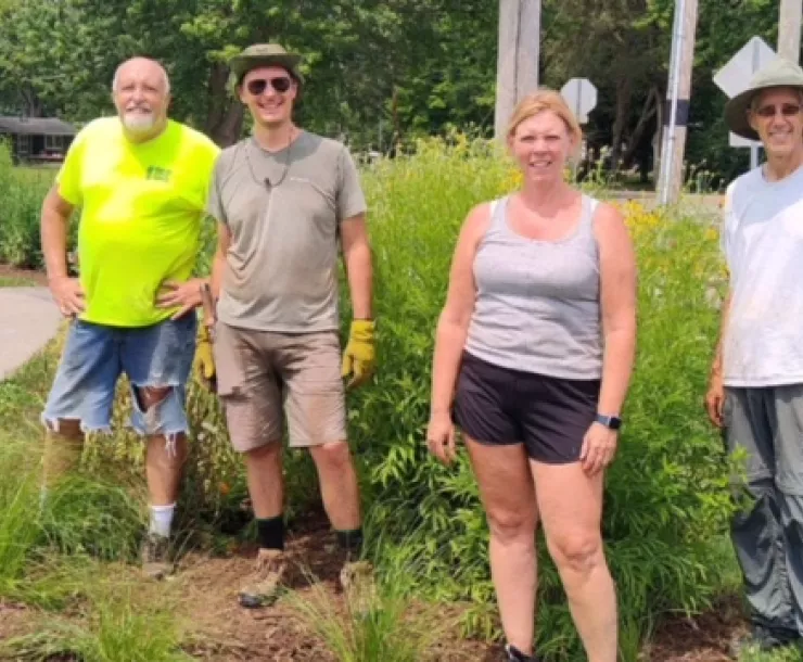 Five people stood by a path with pollinator plants behind them. It's a warm day and most are wearing shorts. They're smiling for the photo and ready to get to work maintaining the path.