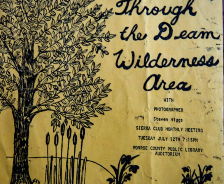 A flyer stating Photographic journey through the Deam Wilderness area with photographer Steven Higgs. Sierra Club monthly meeting. Tuesday July 12 7.15pm. Monroe County Public Library auditorium. The paper is yellow and there is a black ink drawing of a tree and plants and a pond area.
