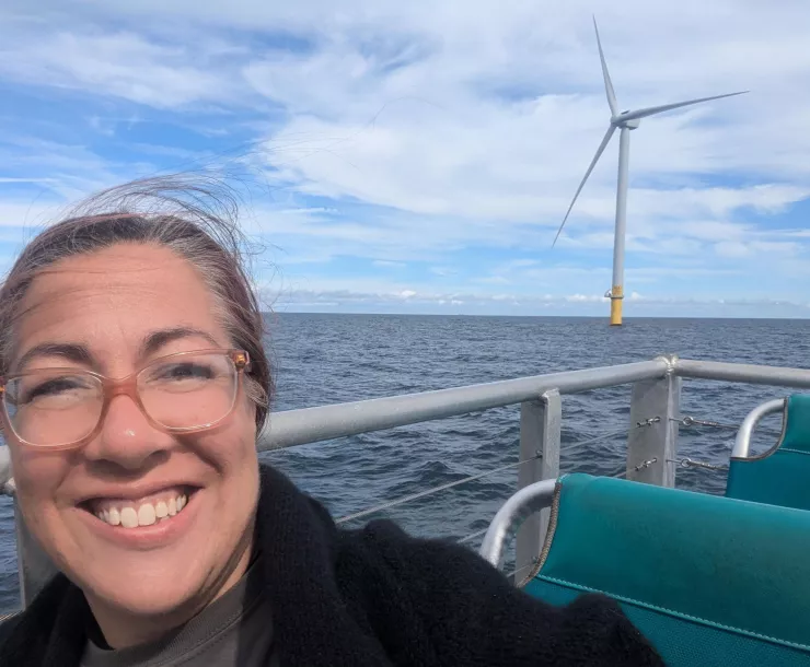 Sam on a boat in front of an offshore wind turbine 